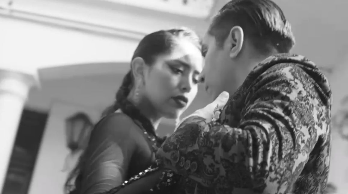 Two dancers held close in an embrace beneath an arch and a wall lantern