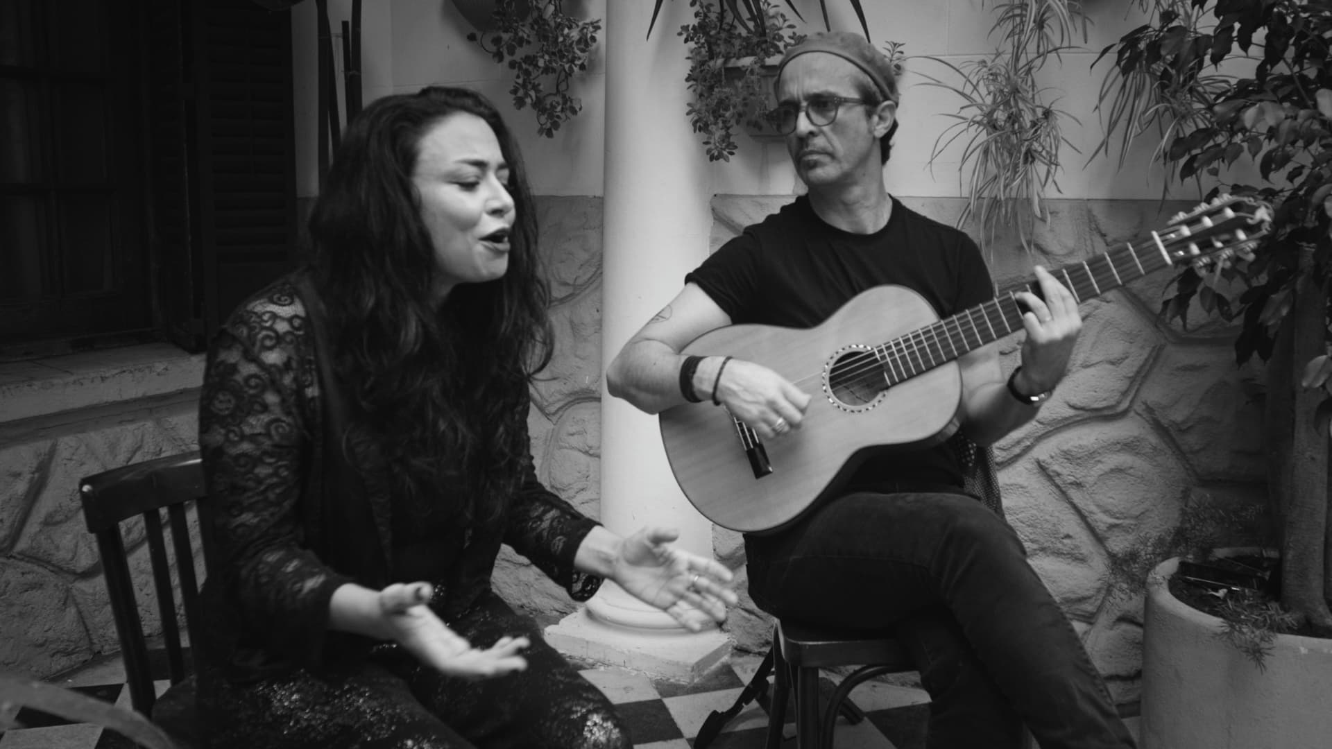 The singer mid-phrase with hands raised while the guitarist plays beside her