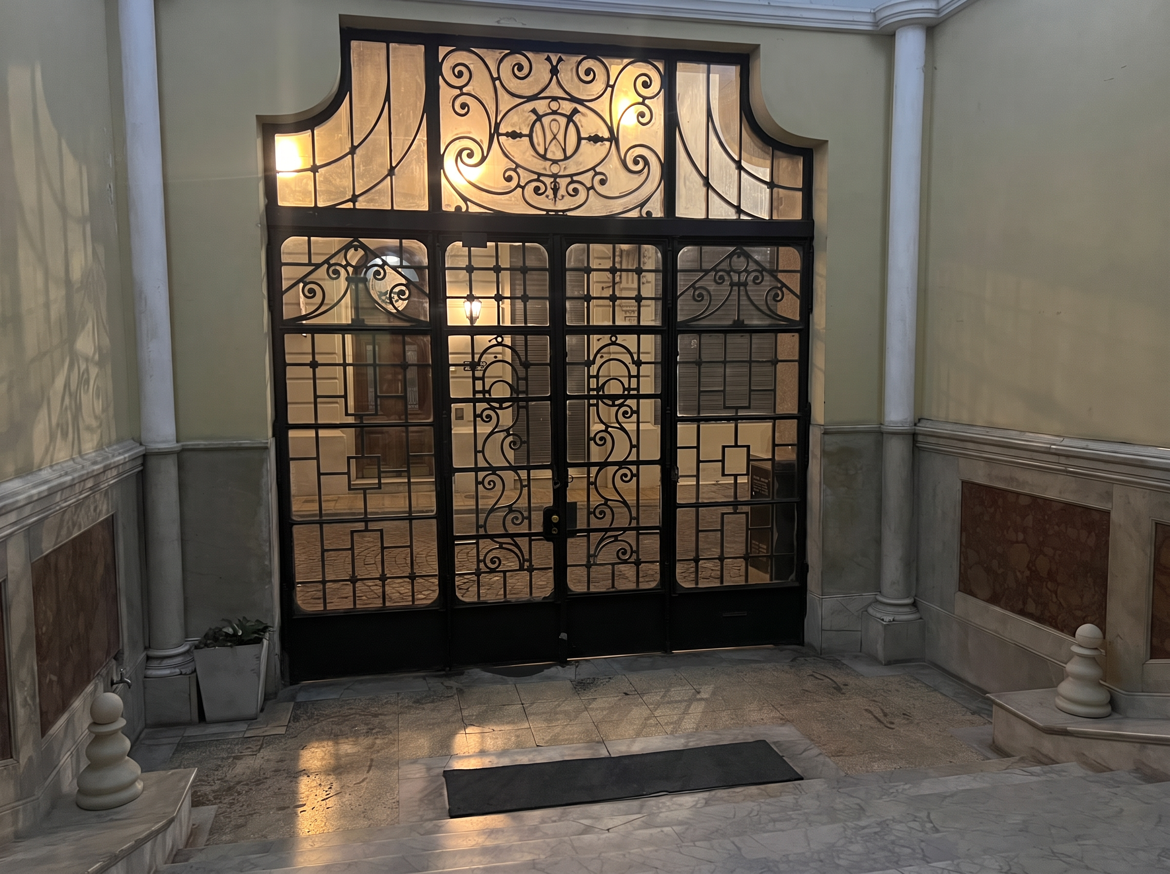 The wrought-iron entrance gate of the building seen from the marble lobby, the street beyond